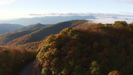 Aerial-view-of-the-blue-ridge-parkway-road-between-the-colorful-fall-mountains-with-the-peaks-covered-in-fog-and-clouds-at-sunset