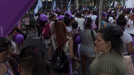 Group-of-feminist-protestors-march-carrying-purple-balloons-and-purple-flags,-they-stay-hydrated-as-they-manifest-on-the-streets-of-Buenos-Aires-during-Women's-Day-celebrations