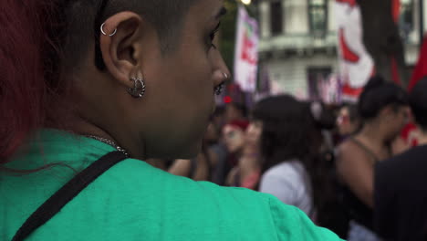 Close-up-back-shot-of-young-female-advocate-during-peaceful-protest,-wearing-green-clothes-and-earrings-with-red-hair