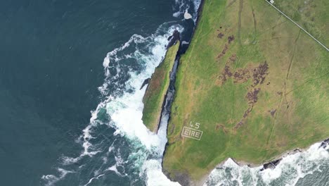 Rugged-Irish-coastline-with-waves-crashing,-marked-with-'ÉIRE'-signat-Loop-Head,-rolling-aerial-shot