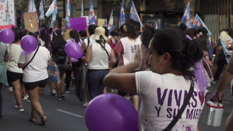 Collective-group-of-women-march-carrying-purple-balloons,-peacefully-manifest-as-they-walk-the-streets-of-Buenos-Aires-to-protest-during-Women's-day-rally