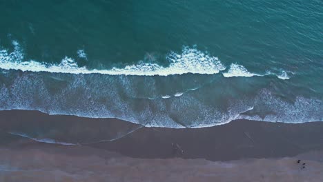 Luftaufnahme-Von-Schaumigen-Wellen,-Die-An-Einen-Sandstrand-Spülen