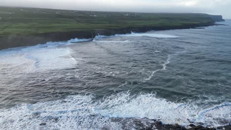 Wilde-Atlantische-Wellen-Krachen-Gegen-Die-Klippen-Von-Doolin,-Irland,-Mit-üppigen-Grünen-Feldern-Im-Hintergrund,-Luftaufnahme