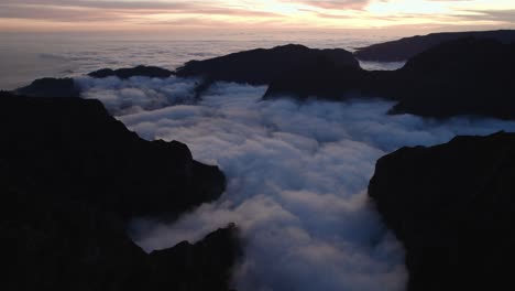 Drone-flying-over-the-clouds-at-sunset-at-Pico-Do-Arieiro,-Madeira-through-mountains