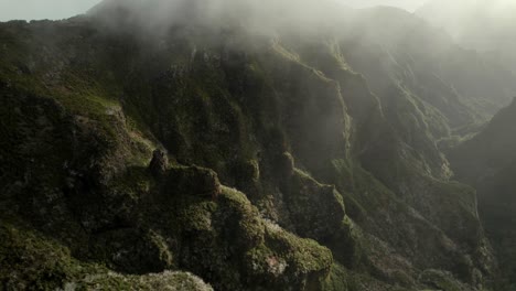 Drone-flying-in-the-mountains-at-Madeira-between-rugged-steep-rocks-and-misty-ridgelines-during-sunrise