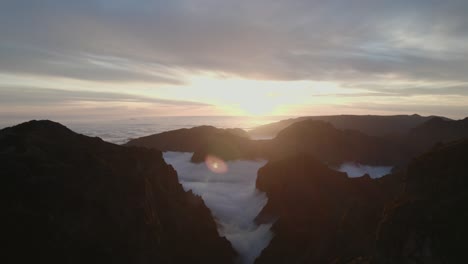 Drone-flying-over-the-clouds-at-sunset-at-Pico-Do-Arieiro,-Madeira-through-mountains