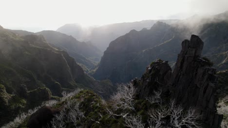 Drone-flying-in-the-mountains-at-Madeira-between-rugged-rocks-and-misty-ridgelines-during-sunrise