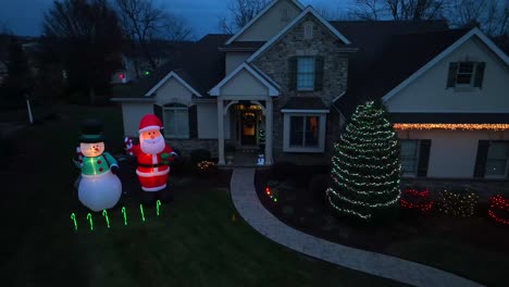Twilight-Christmas-decoration-at-a-stone-front-house-with-inflatable-Santa-and-snowman-and-holiday-lights