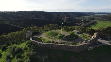 Umlaufende-Aufnahme-über-Der-Burg-Von-Aljezur,-Portugiesische-Flagge-Weht-Im-Wind,-Portugal