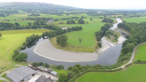 Beautiful-drone-footage-slowly-descending-from-400-feet-and-moving-forward-showing-a-shallow,-slow-moving-meandering-river-in-rural-Lake-District,-UK
