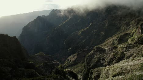 Drone-flying-in-the-mountains-at-Madeira-between-rugged-steep-rocks-and-misty-ridgelines-during-sunrise