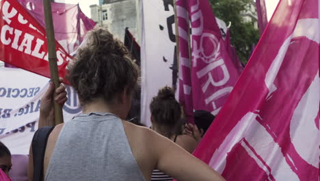 Back-of-female-leftist-protester-hold-waving-pink-and-red-flags-in-a-feminist-rally-during-International-Women's-rights-day