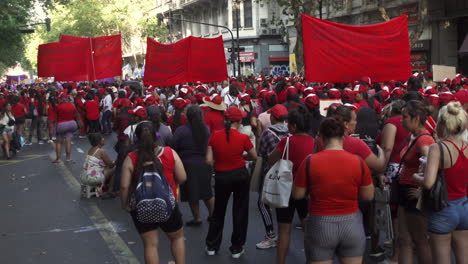 protestors-in-march,-wait-with-signs-and-posters,-dressed-in-red-to-manifest-at-public-street-gathering