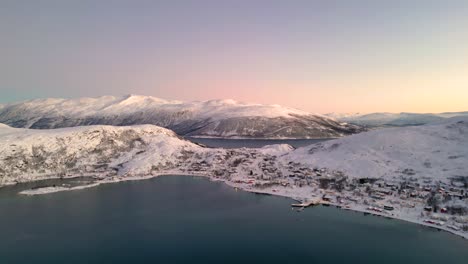 Ersfjordvegen-village-surrounded-by-snow-capped-mountains-during-golden-hour,-aerial-view