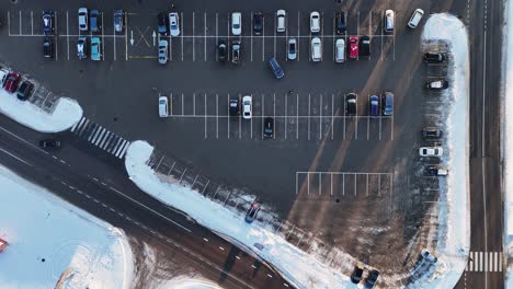 City-parking,-vehicles-leaving-the-parking-lot-seen-from-above-on-a-winter-day