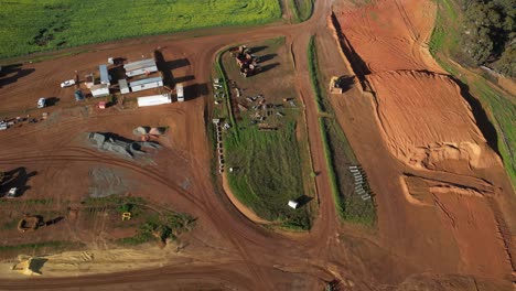 Mining-site-with-red-soil-and-parked-trucks-in-Western-Australia,-aerial-orbital