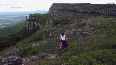 Hispanic-woman-in-colourful-dress-runs-on-cliff-top-trail-at-viewpoint