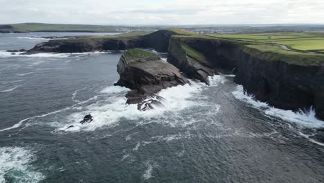Blick-Auf-Die-Klippen-Von-Kilkee-In-Irland-Mit-Wellen,-Die-Gegen-Die-Felsen-Schlagen,-Darüber-Bewölkter-Himmel