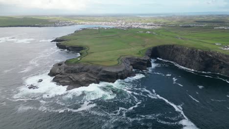 Kilkee-Cliffs-in-Ireland-with-crashing-waves-and-lush-green-landscapes,-aerial-view