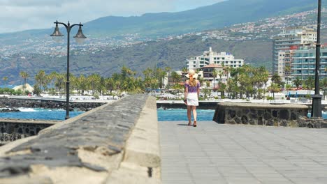 Caucasian-female-walking-down-beautiful-promenade,-tourist-resorts-in-background