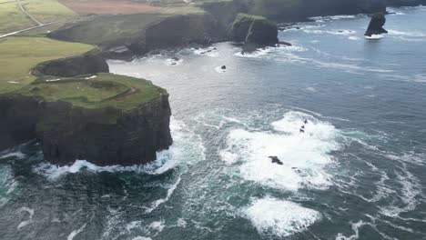 Green-Kilkee-Cliffs-in-Ireland-with-waves-crashing-against-rocks,-aerial-view