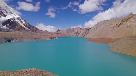 Drone-shot-of-Tilicho-Lake-at-Annapurna-mountain-circuit,-World's-highest-altitude-lake-under-blue-cear-sky-with-clouds,-mountains,-happy-nature,-chilly-weather-Nepal-4K