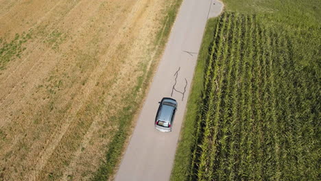 Aerial-follow-up-of-a-car-moving-on-the-road-near-the-agricultural-field-bathed-in-low-angle-sunlight-showcases-the-essence-of-farming-and-agriculture
