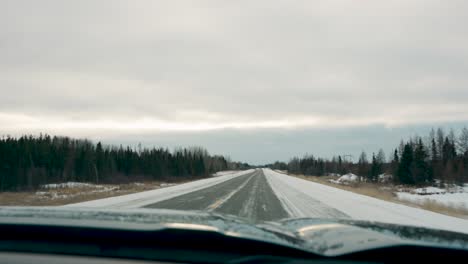 Car-Mounted-Camera-Driving-Shot-Overcast-Sky-Down-a-Winter-highway-Forest-Arctic-Landscape-Seen-Through-a-Windshield-near-Thompson-Manitoba-Canada