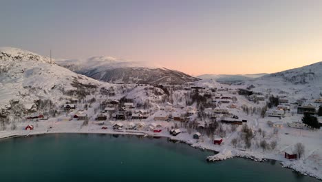 Verschneites-Dorf-An-Einem-Zugefrorenen-See-Bei-Sonnenaufgang-Mit-Warmem-Licht,-Das-Vom-Wasser-Reflektiert-Wird