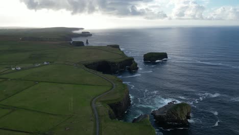 Aerial-view-of-Kilkee-Cliffs-in-Ireland-with-lush-greenery-and-a-meandering-road-at-dusk