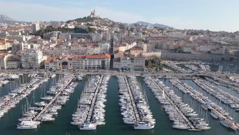 Drone-Shot-of-Marseille,-France,-Yachts-and-Sailboats-in-Old-City-Port,-Coastal-Traffic-and-Cityscape-Skyline