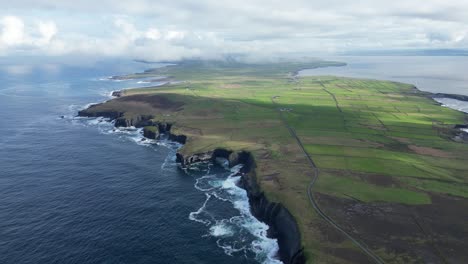 Loophead-peninsula-with-dramatic-cliffs-and-lush-green-fields-under-a-cloudy-sky,-aerial-view