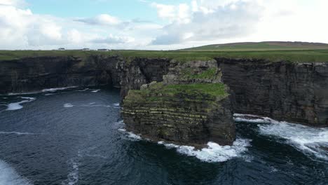 Majestic-Kilkee-Cliffs-on-a-cloudy-day,-waves-crashing-against-the-rugged-coastline,-aerial-view