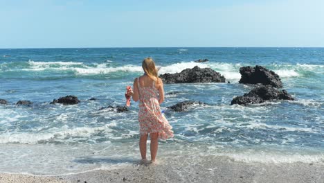 Woman-in-a-summer-dress-on-a-vacation-in-Tenerife,-standing-on-a-beach