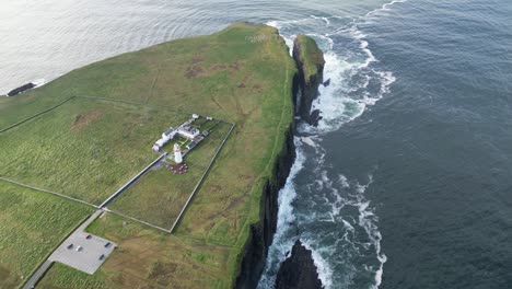 Loophead-lighthouse-on-cliff,-waves-crashing-on-rugged-coastline,-serene-and-remote,-aerial-view