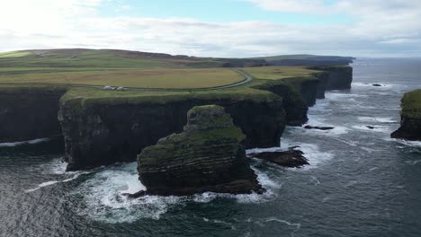 Aerial-view-of-majestic-cliffs-by-the-sea-with-waves-crashing,-under-a-wide-sky