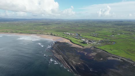 Coastline-with-verdant-fields-and-a-sandy-beach-under-a-blue-sky-with-clouds-at-dughmore-bay