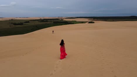 Aerial-orbits-Latina-in-red-dress-walking-w-dog-on-Bolivia-sand-dune