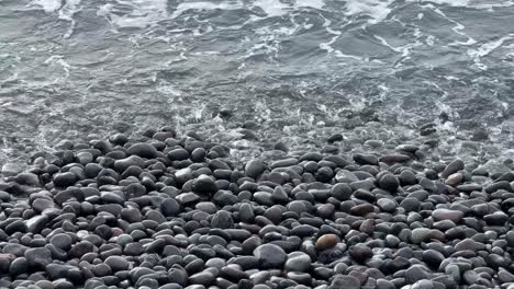 Sea-water-waves-into-rocky-pebble-stone-beach,-relaxing-calming-in-Tenerife