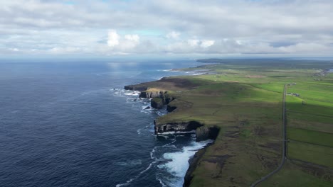 Loophead-peninsula-with-dramatic-cliffs-against-the-Atlantic,-lush-greenery,-and-cloudy-skies,-aerial-view