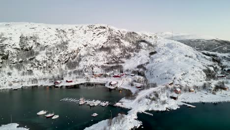 Snowy-coastal-village-with-boats-and-docks-during-winter,-aerial-view