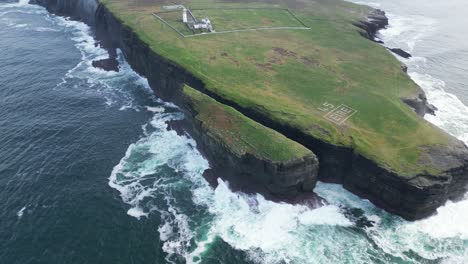 Aerial-view-of-rugged-coastline-with-"ÉIRE"-sign,-waves-crashing-on-cliffs,-historical-marker