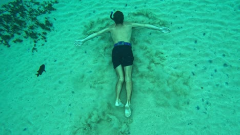 Man-swims-along-sandy-bottom-of-deep-ocean-water-as-sand-floats-from-his-paddling