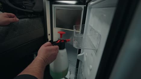 Mobile-truck-interior-cleaning-as-an-unrecognizable-man-meticulously-cleans-the-fridge-using-a-specialized-cleaning-spray