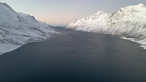 Schneebedeckte-Berge-Flankieren-In-Der-Dämmerung-Einen-Ruhigen-Fjord-Und-Deuten-Auf-Das-Friedliche-Ende-Eines-Klaren-Tages-Hin