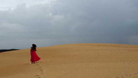 Long-hair-Hispanic-woman-in-long-red-dress-runs-up-huge-sand-dune