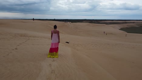 Woman-in-colourful-dress-walks-with-dog-on-sand-dune,-Santa-Cruz-BOL