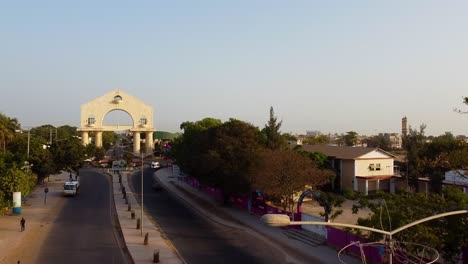 Aerial-tour-over-avenue-towards-Arch-22-portal-in-Banjul,-Gambia