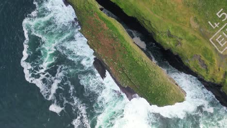 Loophead-peninsula-with-waves-crashing-against-cliffs,-lush-greenery,-aerial-view