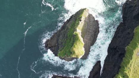 Rugged-Kilkee-Cliffs-meeting-the-Atlantic,-waves-crashing,-greenery-around,-aerial-view